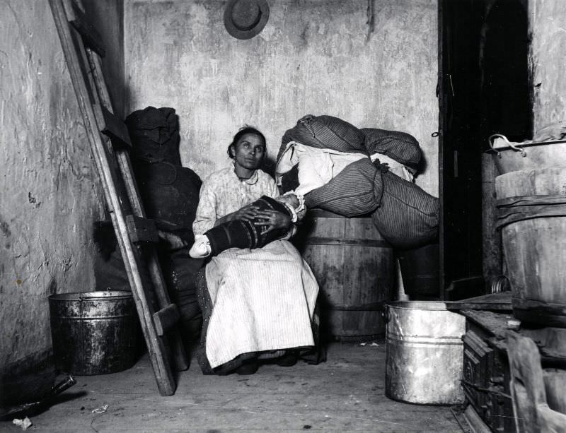 An Italian Immigrant Rag-Picker Sits With Her Baby In A Small Run-Down Tenement Room On Jersey Street, 1887.