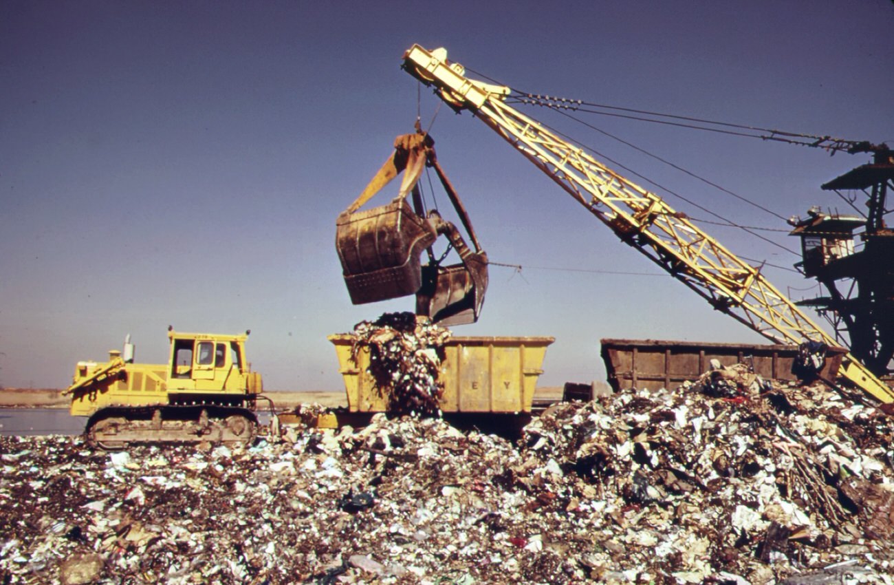 At Staten Island Landfill Steam Shovel Loads Carts With Garbage Brought By Barge From Manhattan. Carts Will Haul Refuse To Outer Edges Of Dumping Area, 1970S