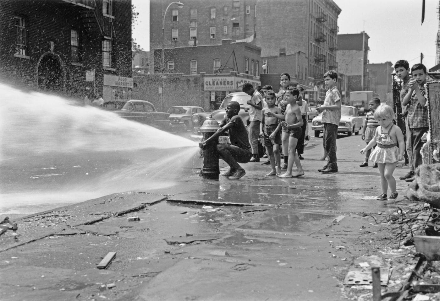 Summer In The City: Children Stand And Watch As A Young Boy Opens A Fire Hydrant In Harlem, Manhattan, 1955