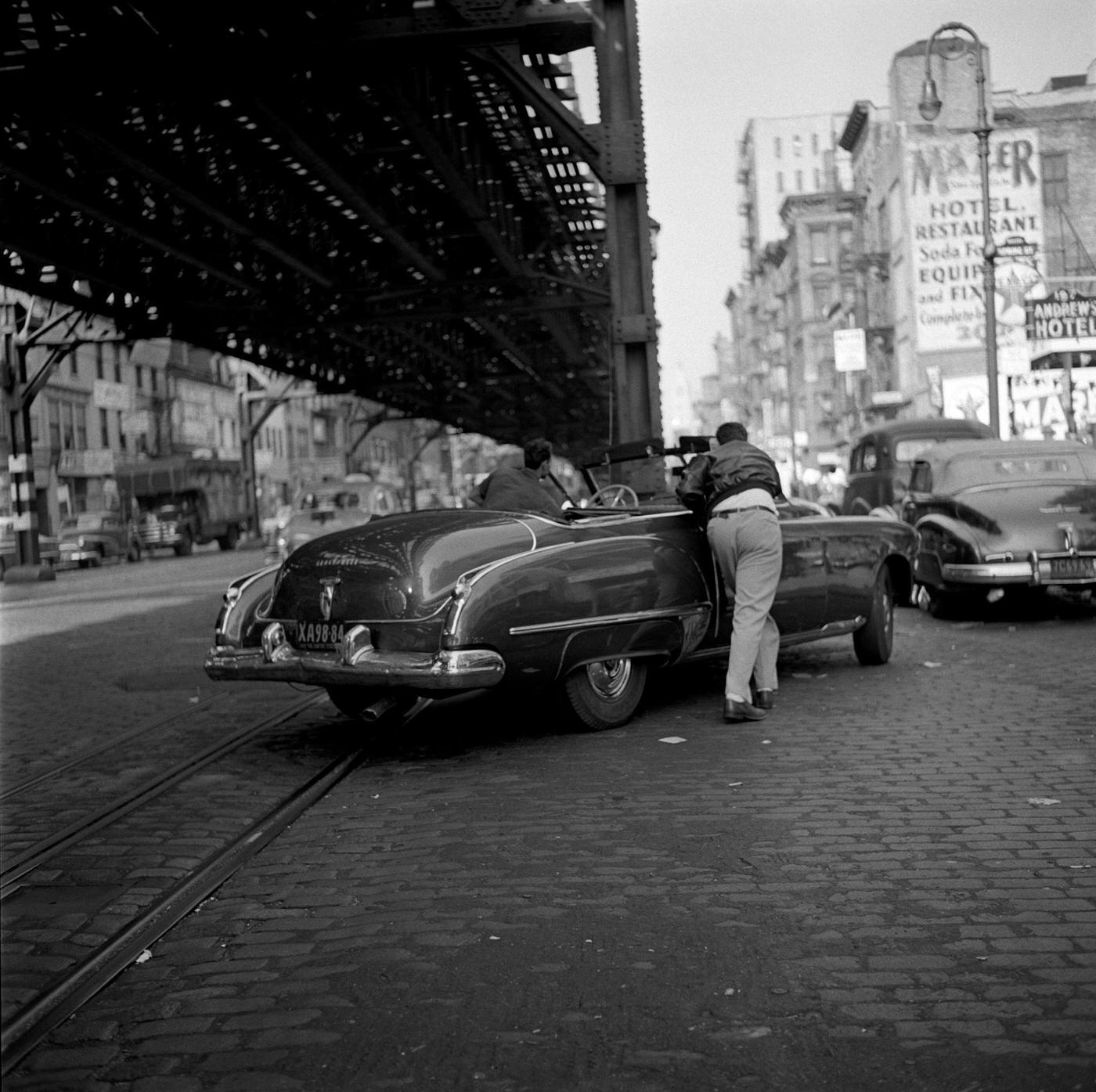 In The Shadow Of The Third Avenue El: Two Men Push A Car Onto Bowery Under The Train In New York, Manhattan, 1954