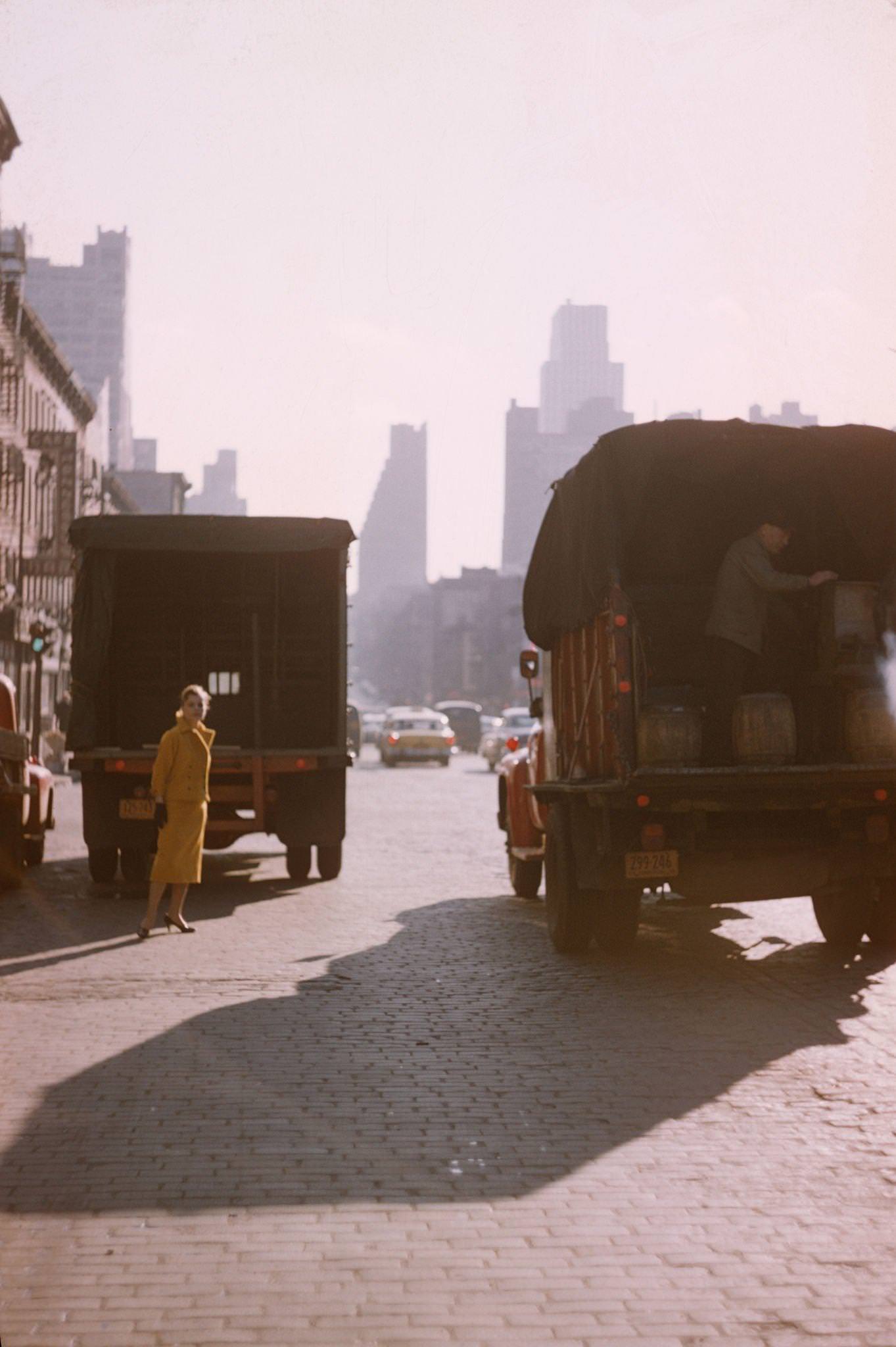 Model In A Yellow Wool Suit Stands Nearby As A Truck Is Unloaded On A Lower Manhattan Street, Manhattan, 1958.