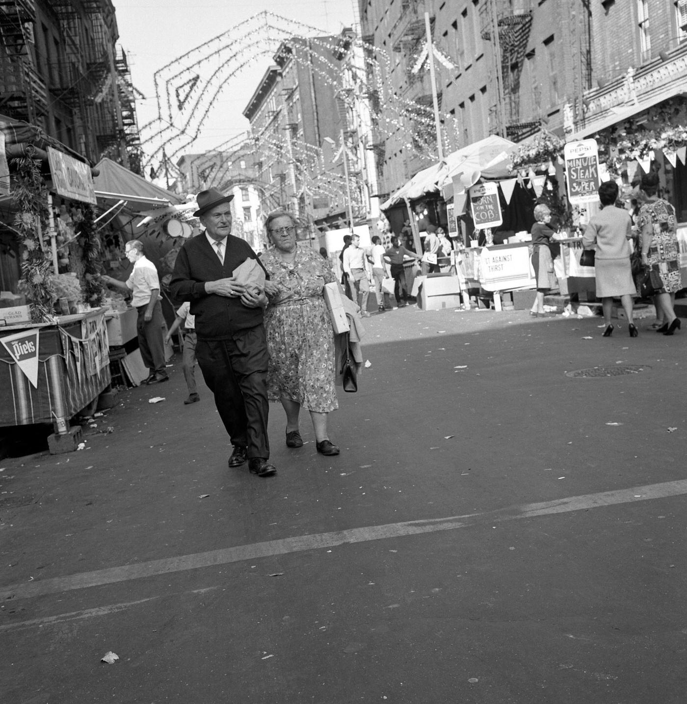 Senior Couple Walking Along Mulberry Street During The Feast Of San Gennaro Festival, Little Italy, Manhattan, 1968.