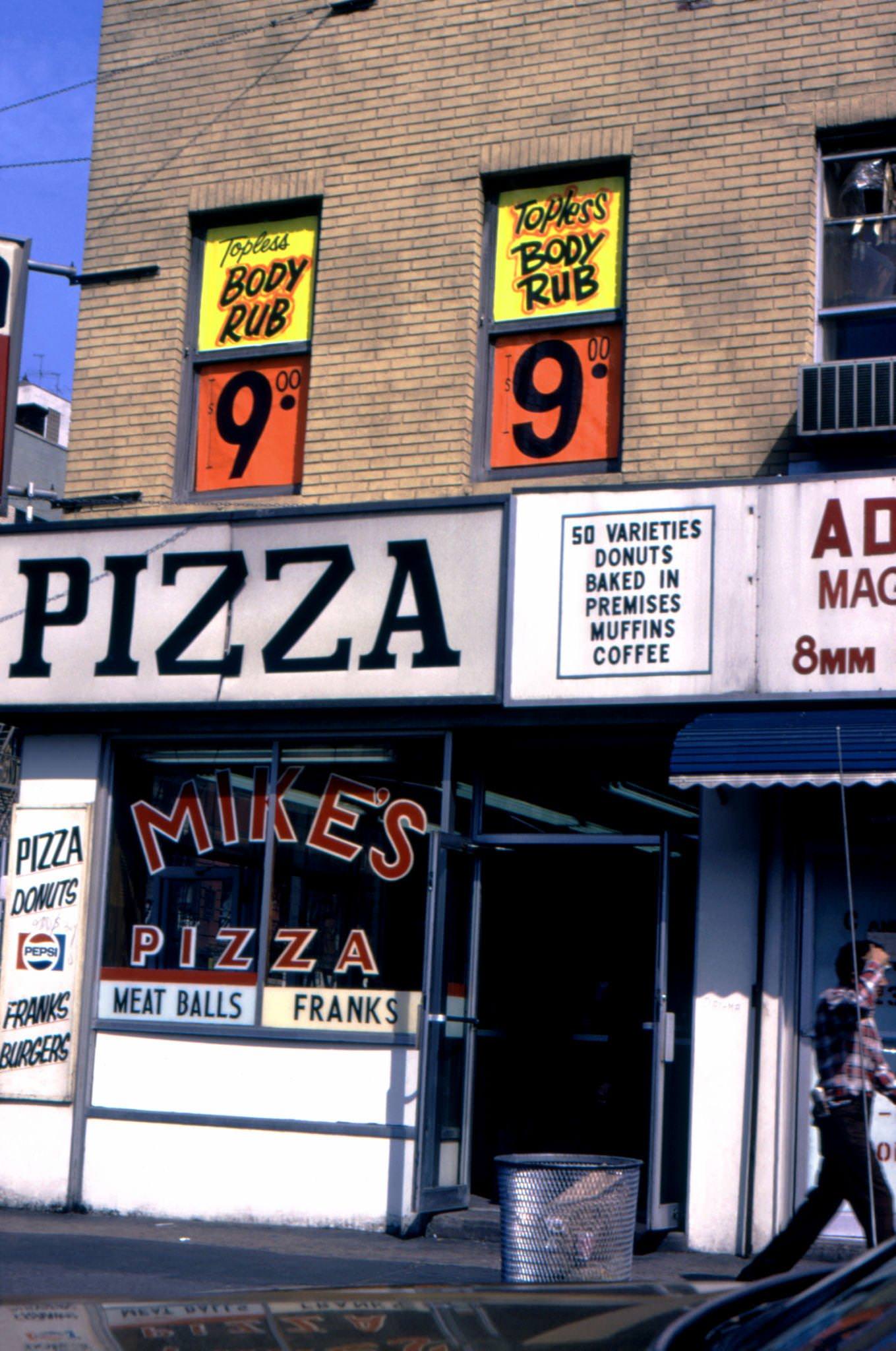 Pedestrian Passes a Pizzeria, Mike's Pizza, and a Topless Massage Parlor in Lower Manhattan, 1975.