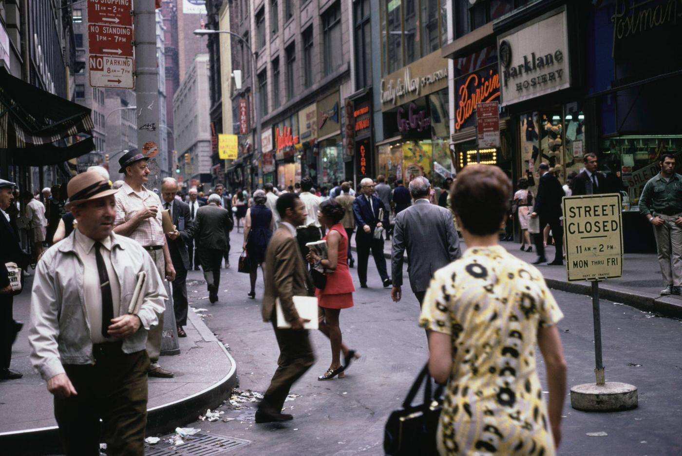 Pedestrians Crossing a Road Lined with Shops in Downtown Manhattan, 1975.