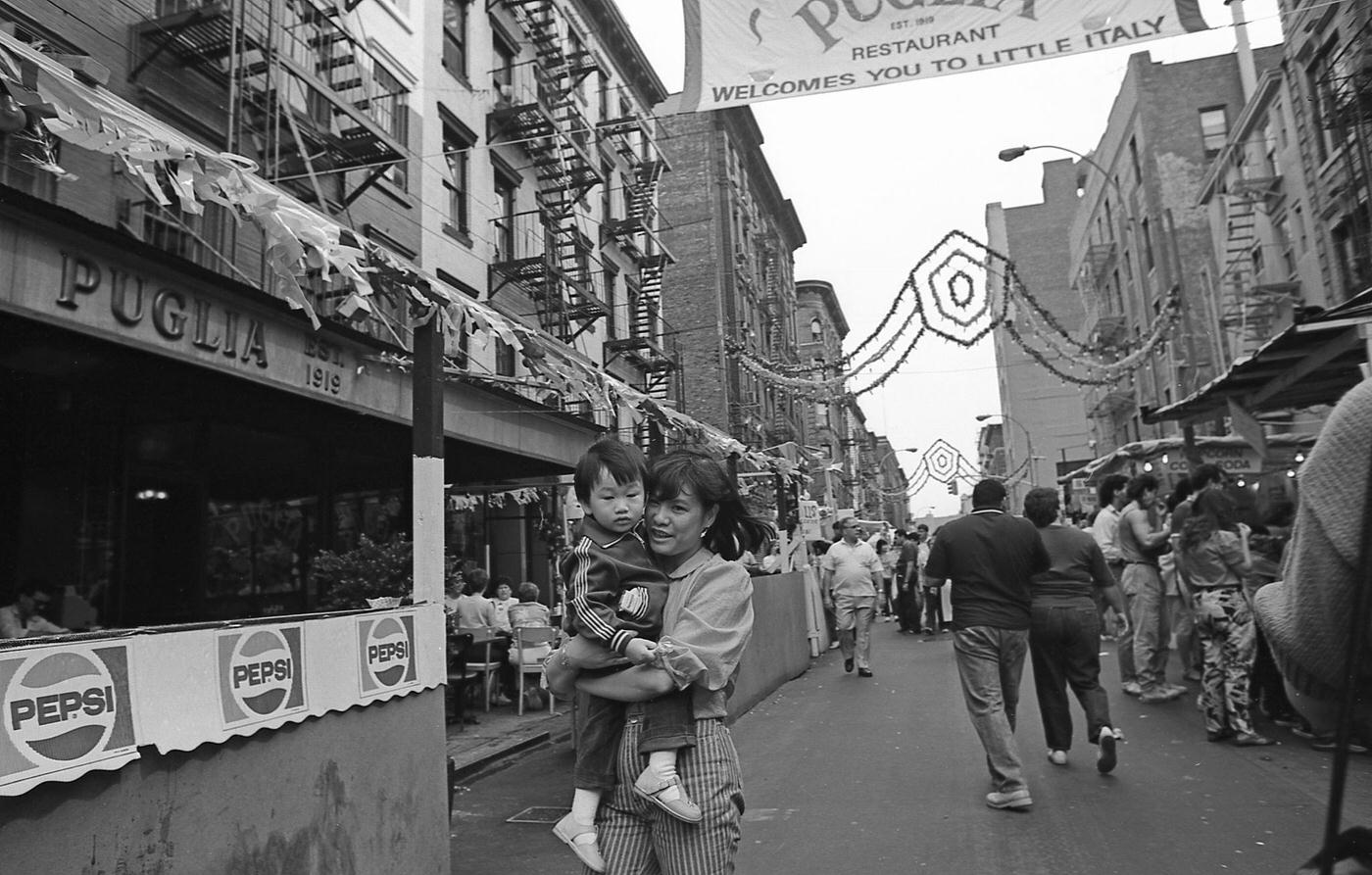 Mother Carrying Child During The San Gennaro Festival, Manhattan, 1986