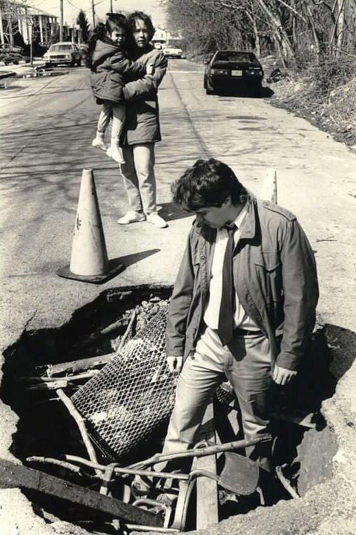 Staten Island Advance Reporter Gauges The Depth Of A Debris-Littered Hole With Onlookers, Location Unknown, 1987.