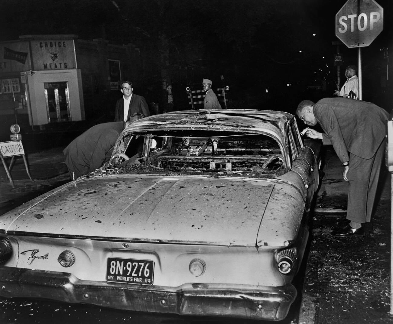 Detective Examines Burned-Out Police Car After A Night Of Rioting In Brooklyn, July 1964.