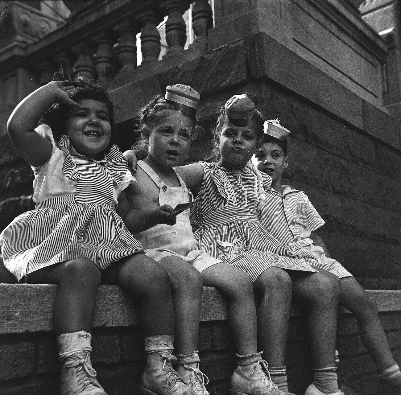 Four Children In Novelty Hats Sitting On A Brick Wall, 1944