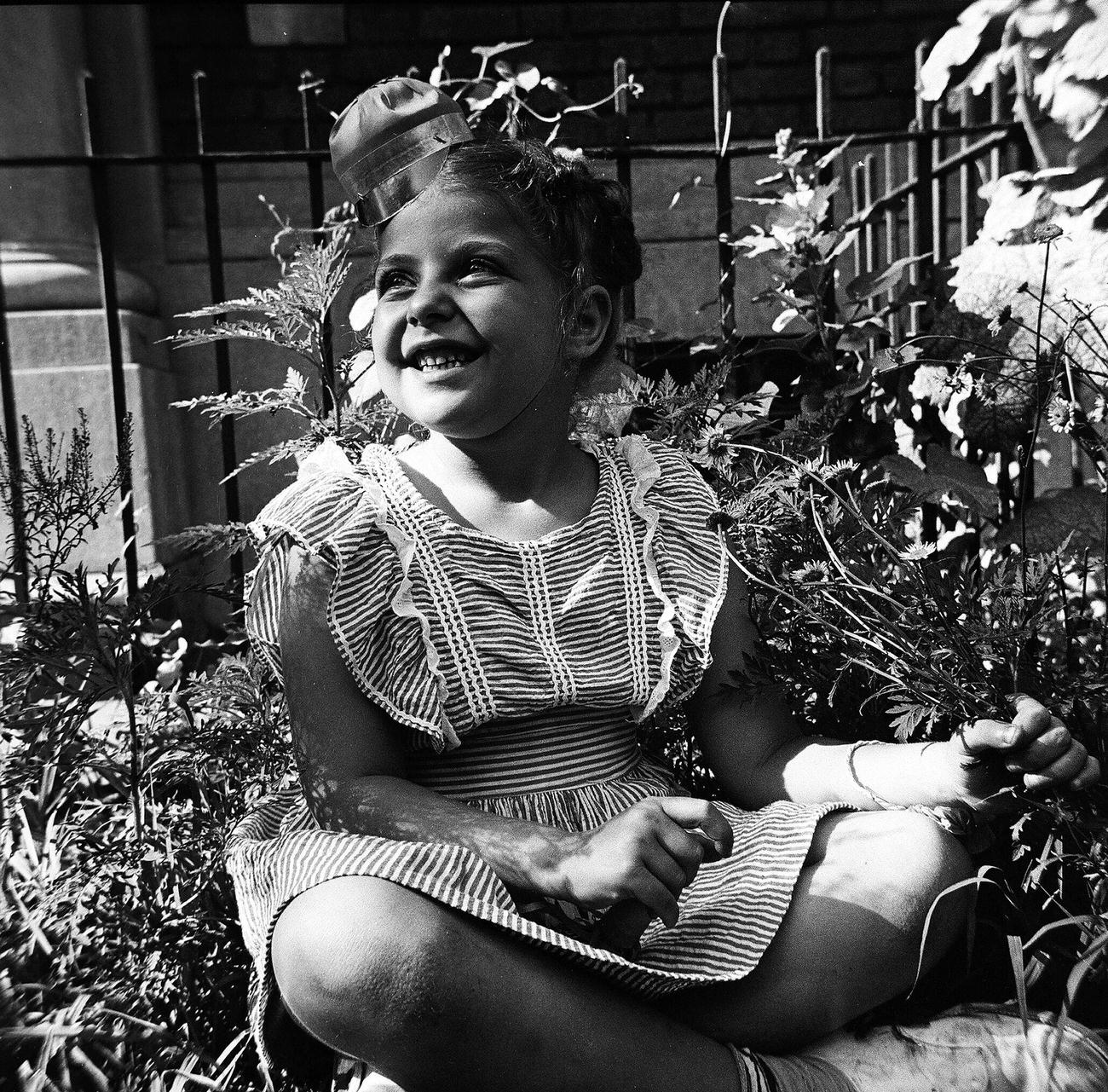 Young Girl In Novelty Hat Sitting In A Garden, 1944