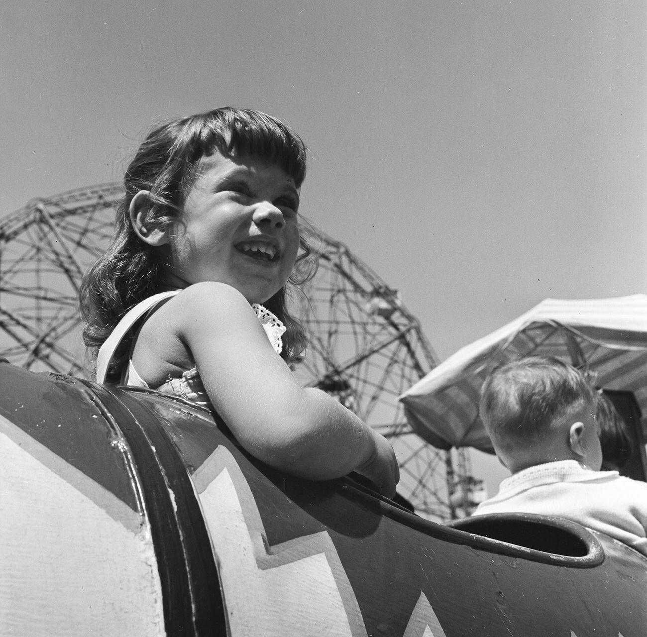 Young Girl Smiles In Anticipation On A Coney Island Ride, Ferris Wheel In Background, 1948