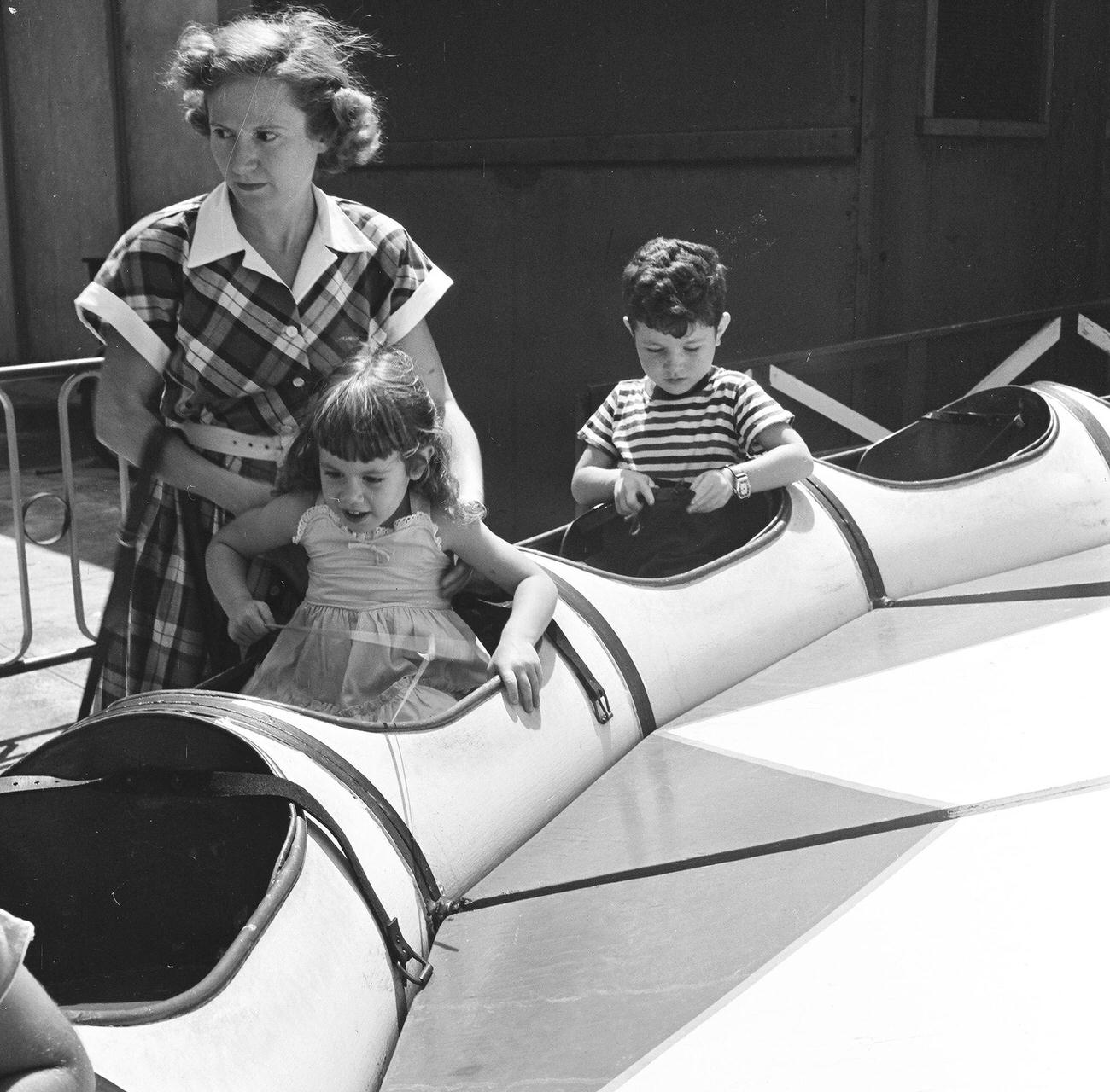 Mother Helps Daughter Board A Ride While Son Adjusts Seatbelt At Coney Island, 1948