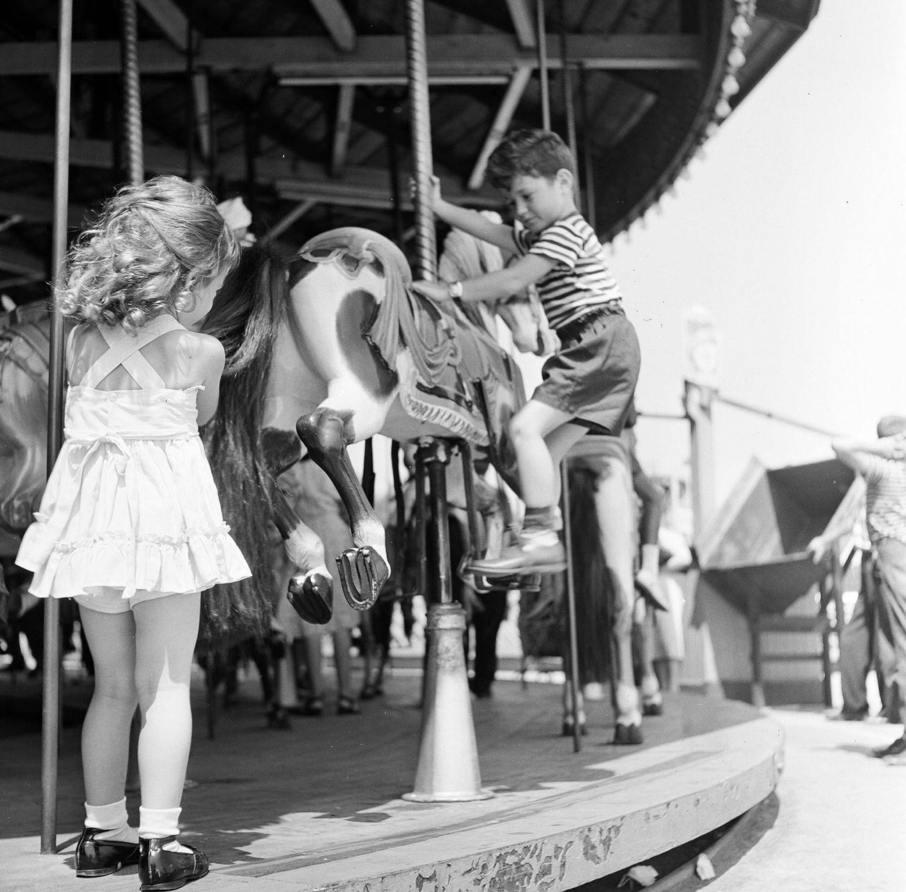 Young Girl Watches Brother Climb Onto Carousel Horse At Coney Island, 1948