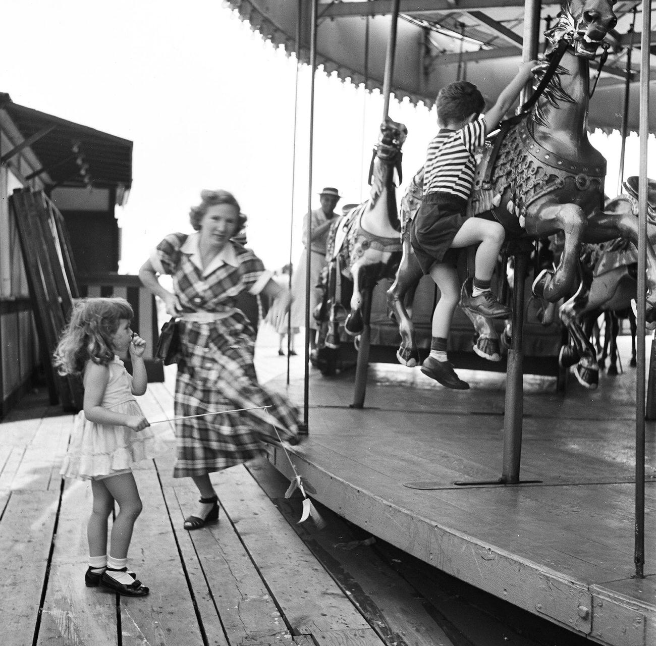 Boy Climbs Onto Carousel Horse As Mother Approaches Sister At Coney Island, 1948