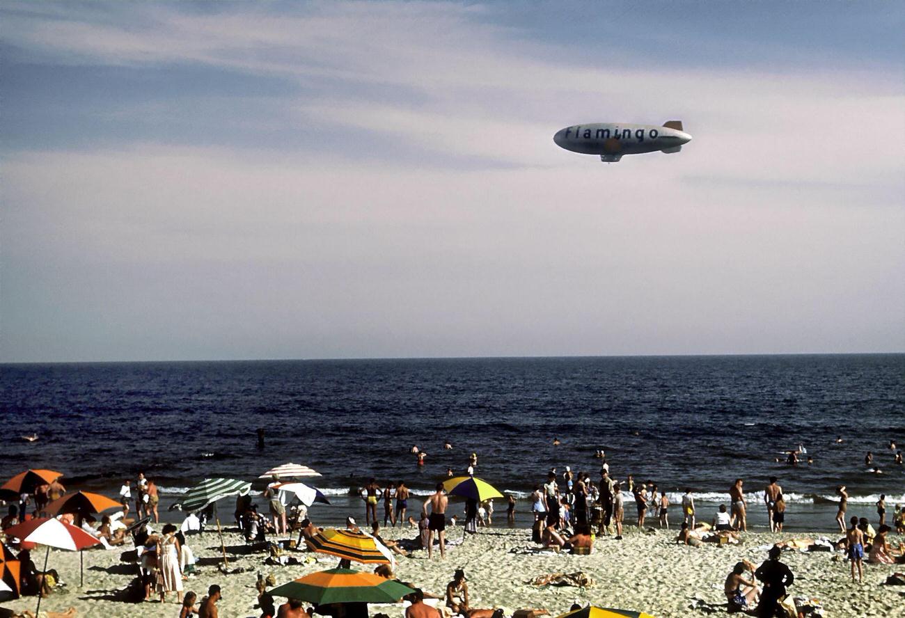 Sunbathers And Swimmers At Coney Island Beach With A Flamingo Blimp Overhead, 1948