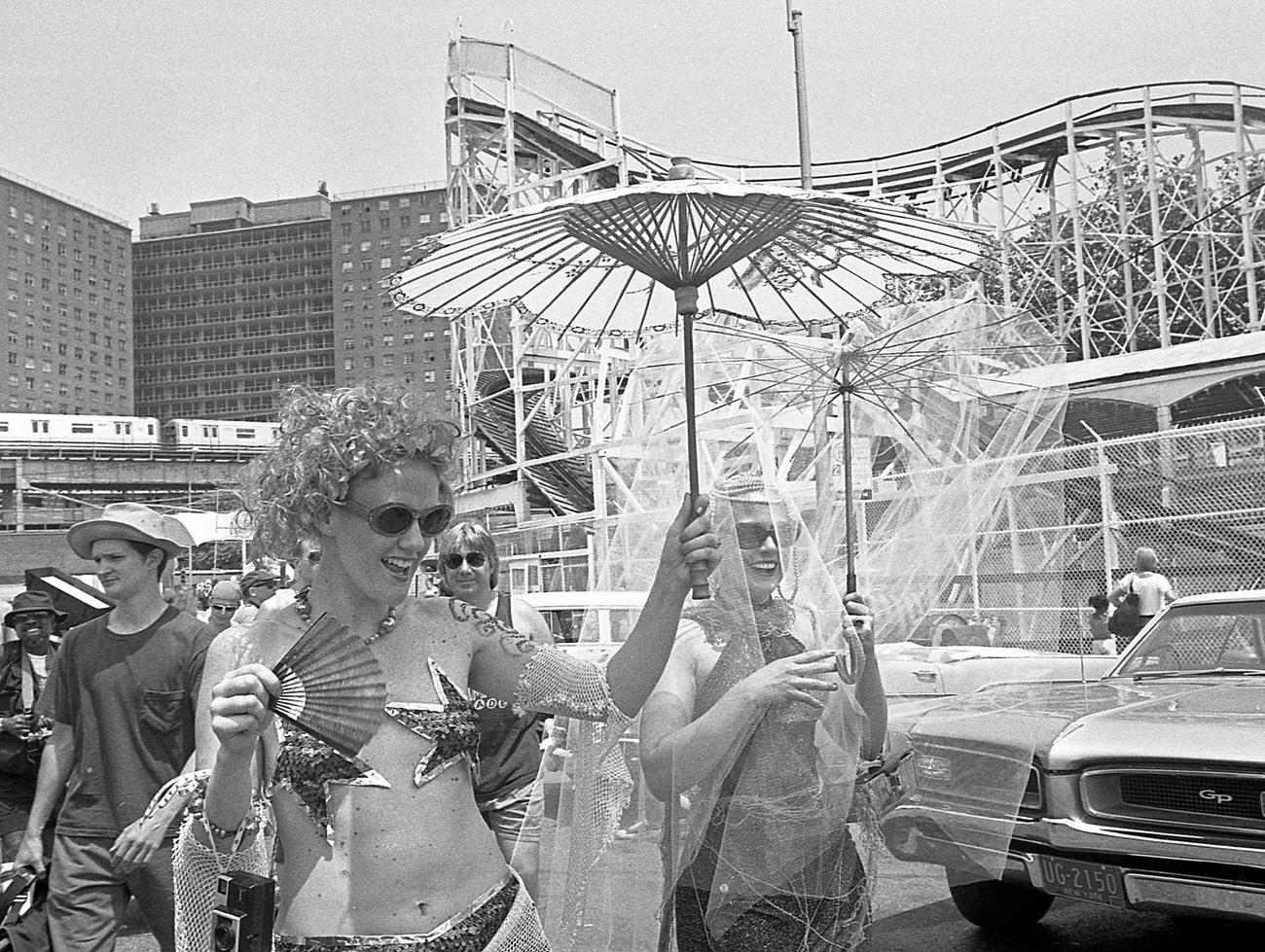 Women Carry Paper Parasols At Coney Island Mermaid Parade, Cyclone Roller Coaster Visible, 1997