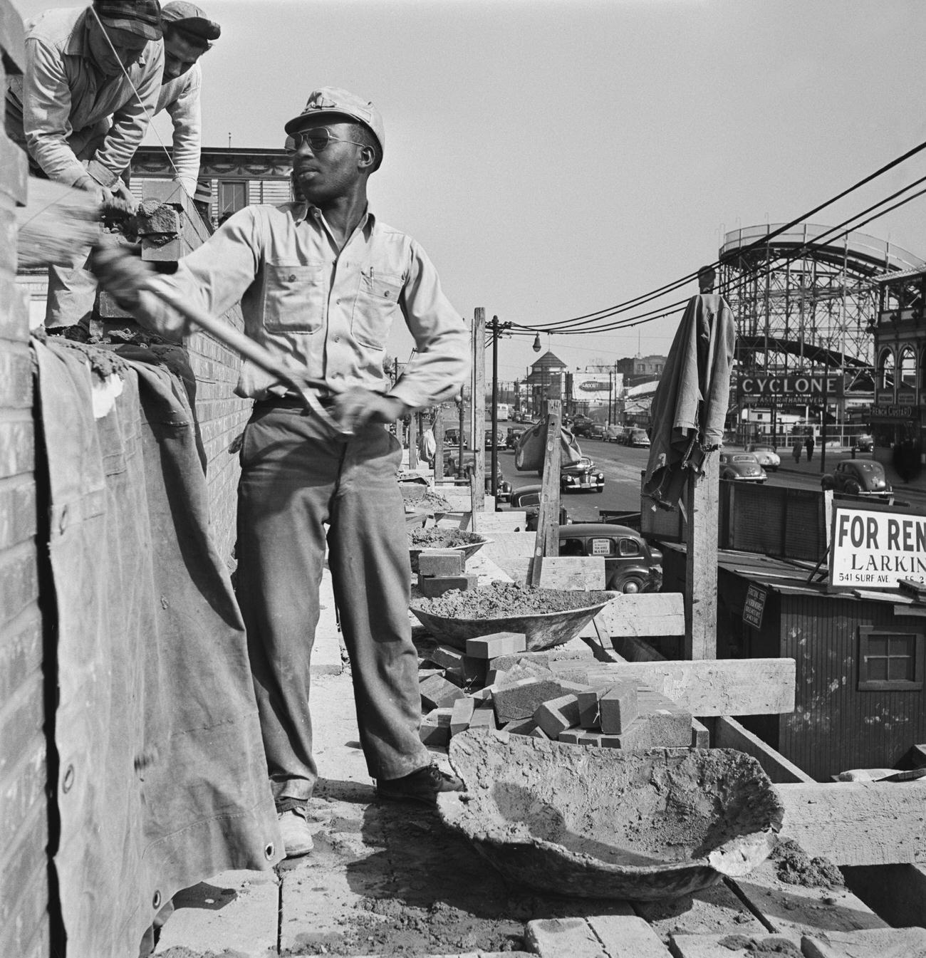 Bricklayer Shoveling Mortar With Cyclone Roller Coaster In Background At Coney Island, 1950