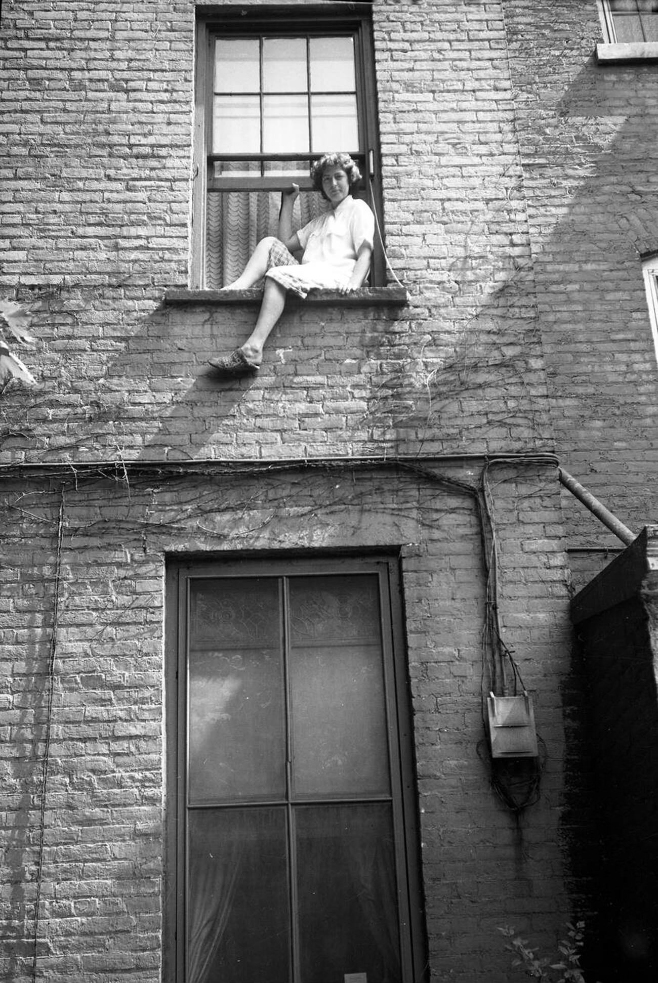 Young Woman Sitting On Tenement Window Ledge In The Bronx.