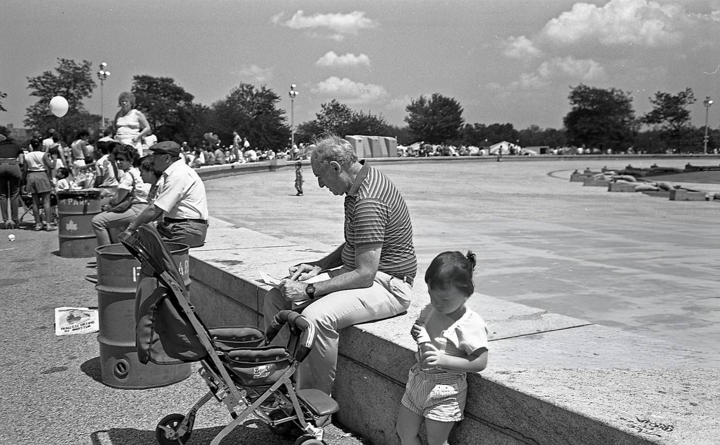 People sit along the stone wall next to the Unisphere in Flushing Meadows Park, Corona, Queens, 1986.