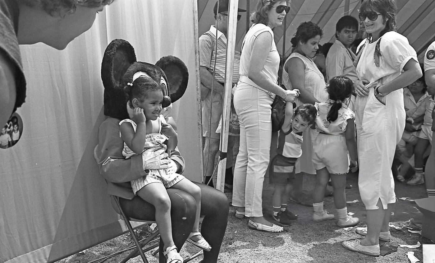 A young girl sits on the lap of 'Mickey Mouse' in Flushing Meadows Park, Corona, Queens, 1986.