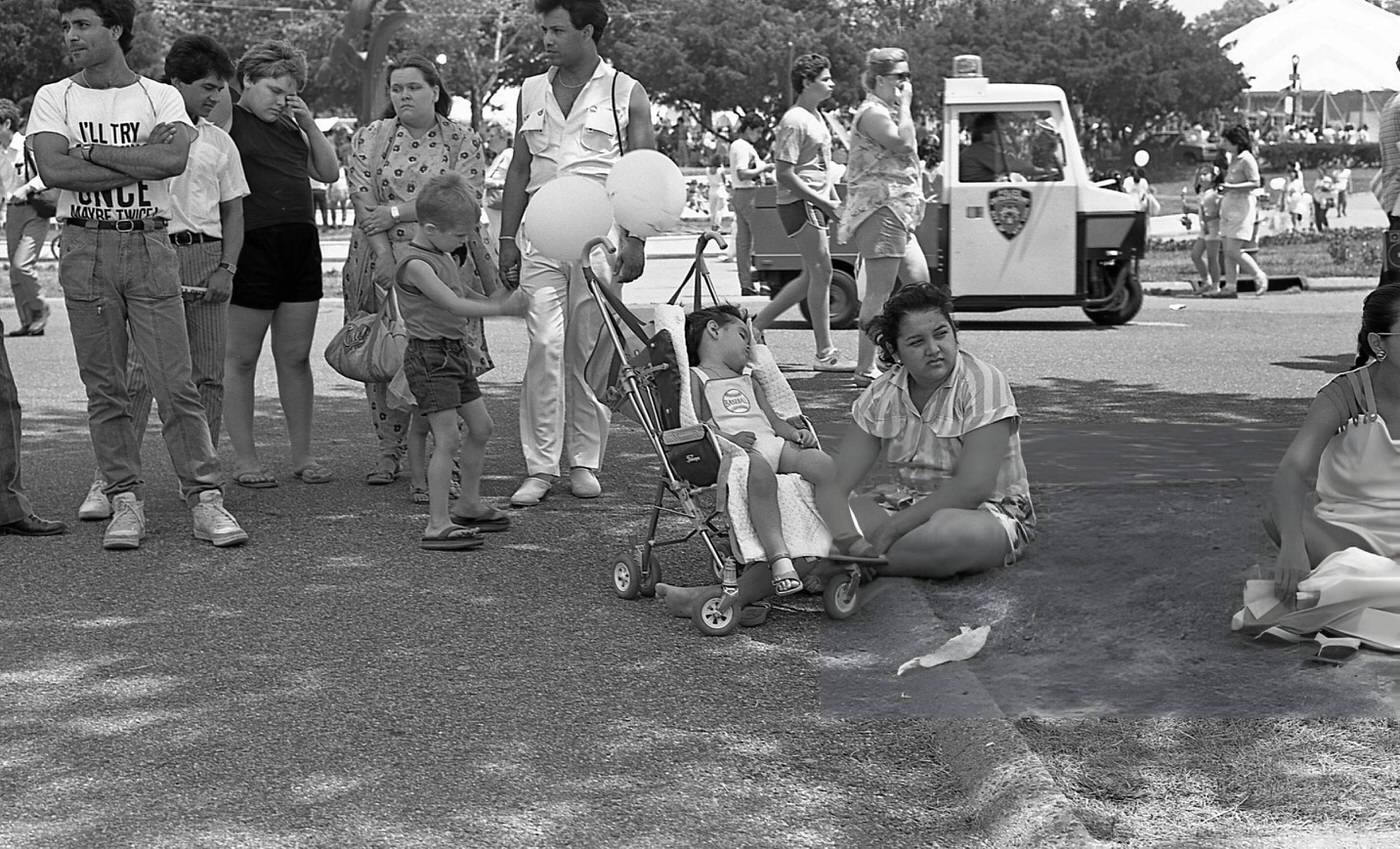 A woman crouches on the grass beside a toddler sleeping in a stroller in Flushing Meadows Park, Corona, Queens, 1986.