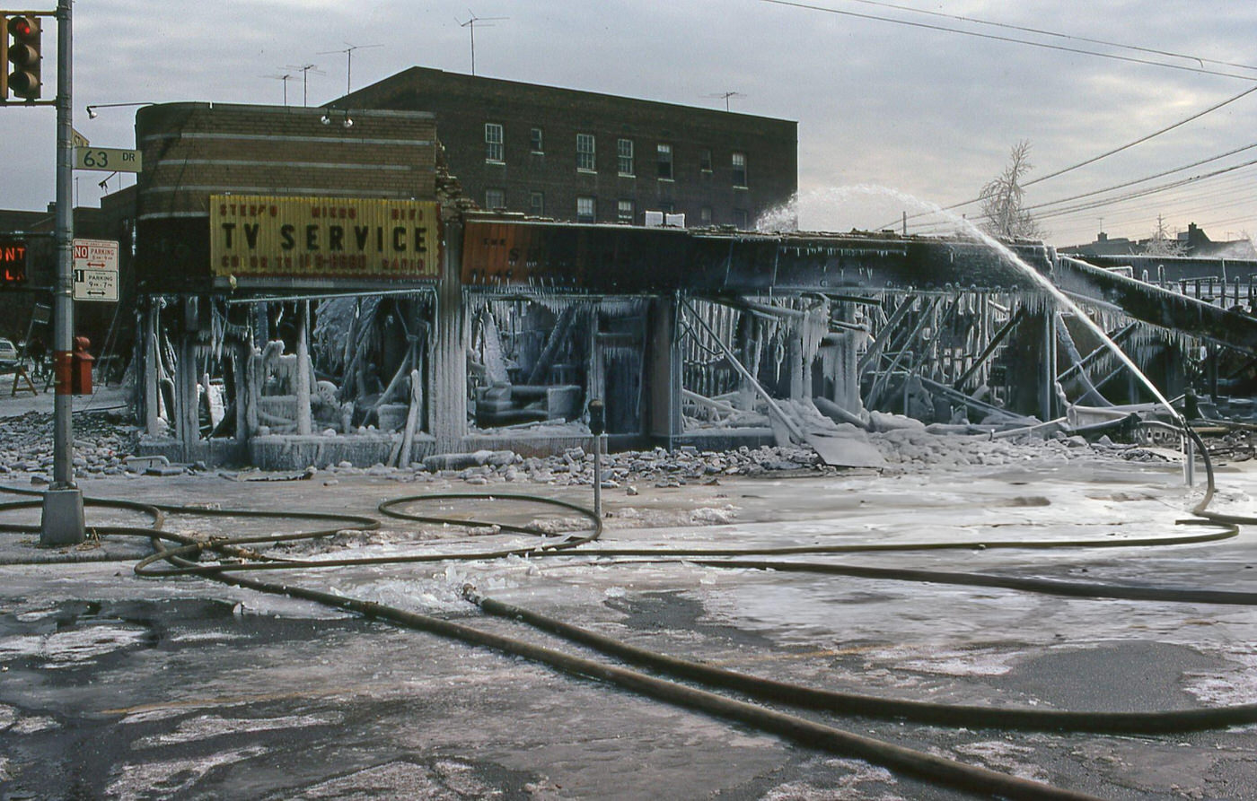 An Unmanned Fire Hose Sprays Water On A Row Of Retail Shops That Were Destroyed By Fire On 63Rd Drive In The Rego Park Neighborhood, Queens, 1970S.