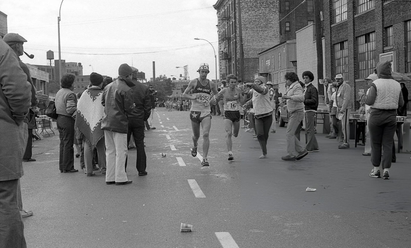 Two Runners Pass The 14-Mile Marker On Crescent Street During The New York City Marathon, Queens, 1980.