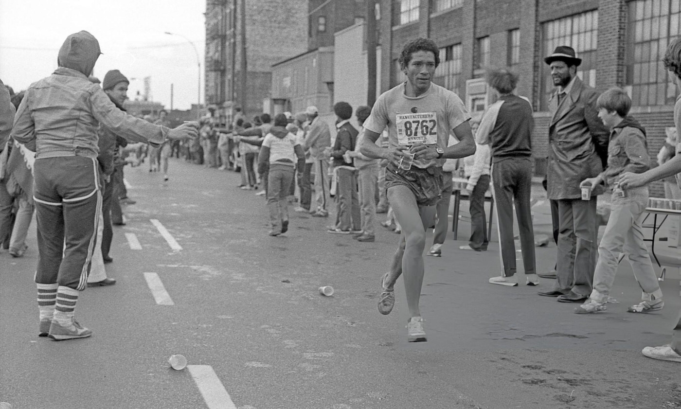 A Runner Holds A Cup Of Water As He Passes The 14-Mile Marker On Crescent Street During The New York City Marathon, Queens, 1980.