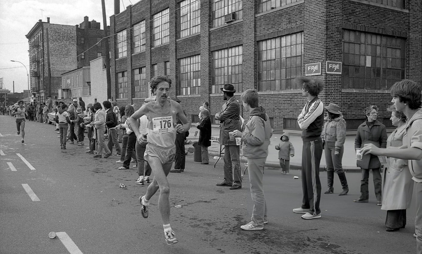 A Runner Passes The 14-Mile Marker On Crescent Street During The New York City Marathon, Queens, 1980.