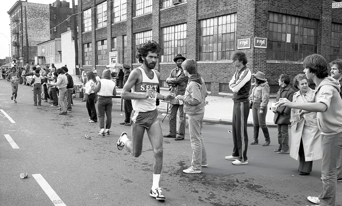 A Runner Passes The 14-Mile Marker On Crescent Street During The New York City Marathon, Queens, 1980.