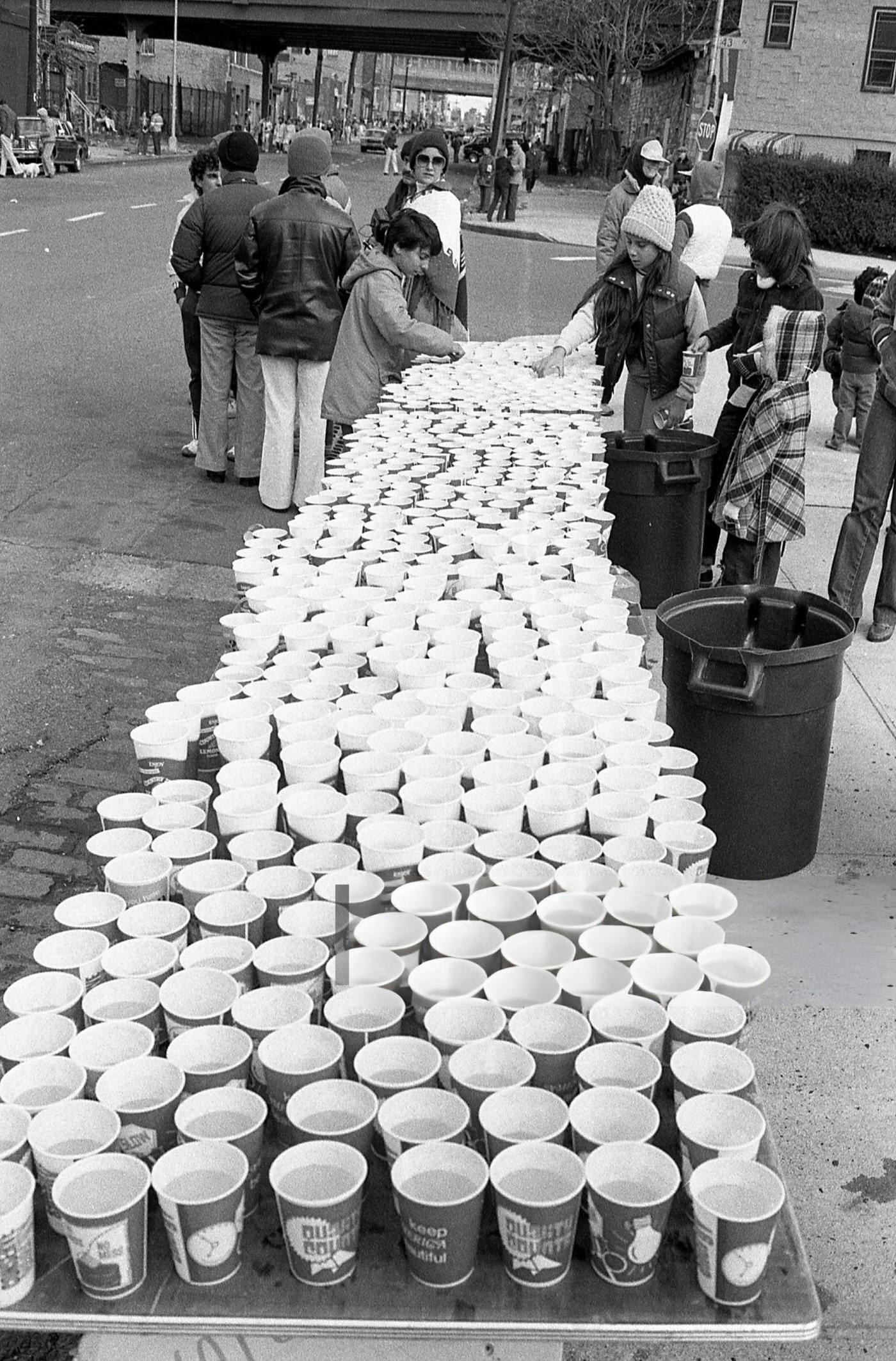 Volunteers at a water station place filled cups on folding tables at the 14-mile marker on Crescent Street during the New York City Marathon, Queens, 1980.