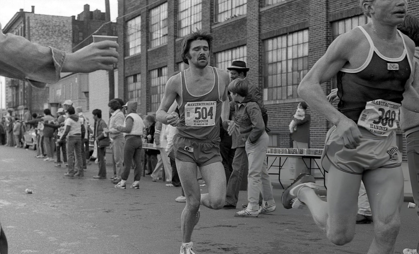 A Runner Passes The 14-Mile Marker On Crescent Street During The New York City Marathon, Queens, 1980.