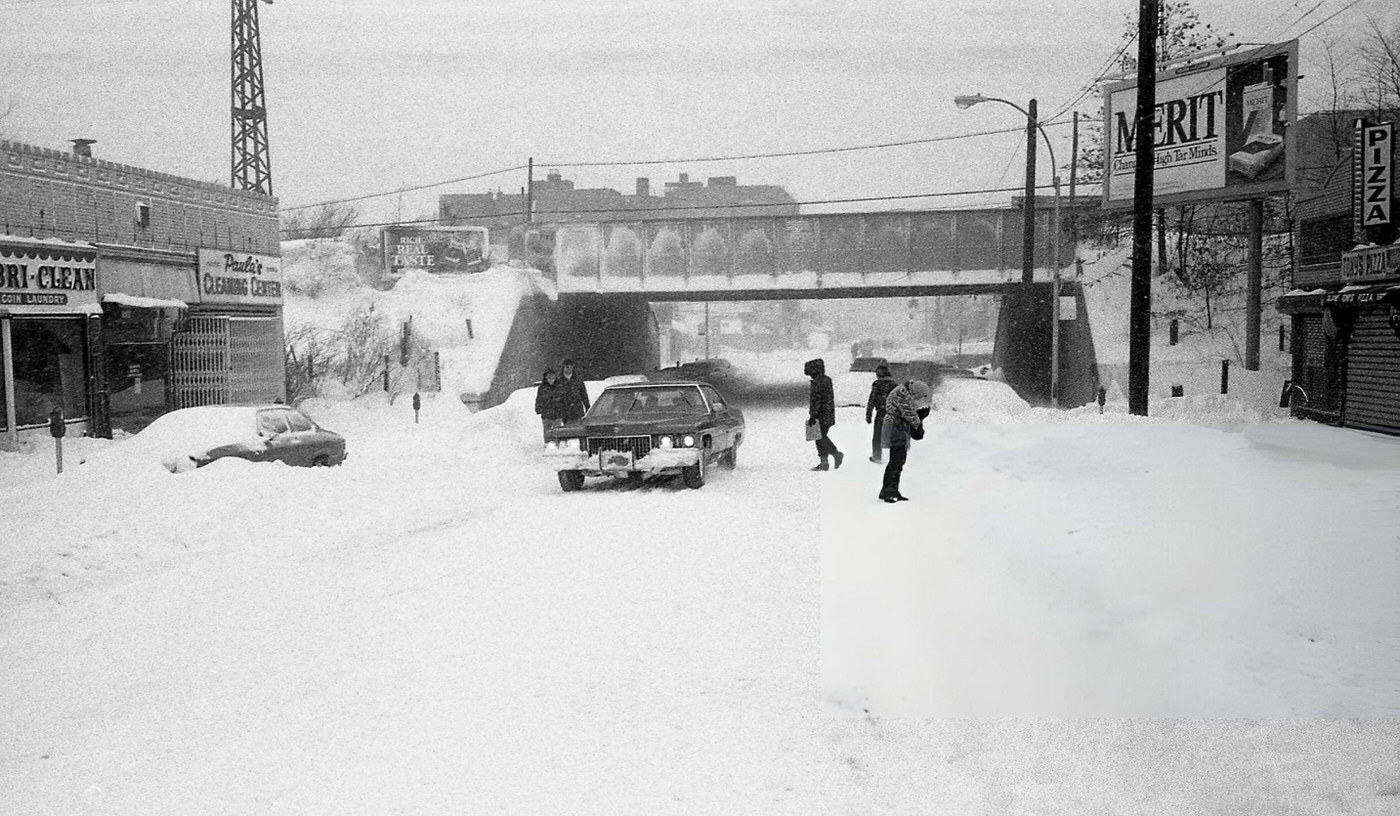 Pedestrians Braving Blizzard Conditions, Walking In The Middle Of The Street In Queens As A Lone Vehicle Navigates Deep Snow During The Height Of The Blizzard Of 1978.