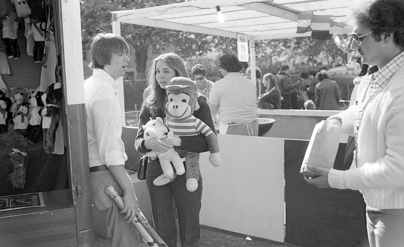 A Young Man Holding Rolled-Up Posters Beside A Young Woman Who Holds Two Stuffed Animals At The Resurrection Ascension Church Carnival In Rego Park, Queens, 1979.