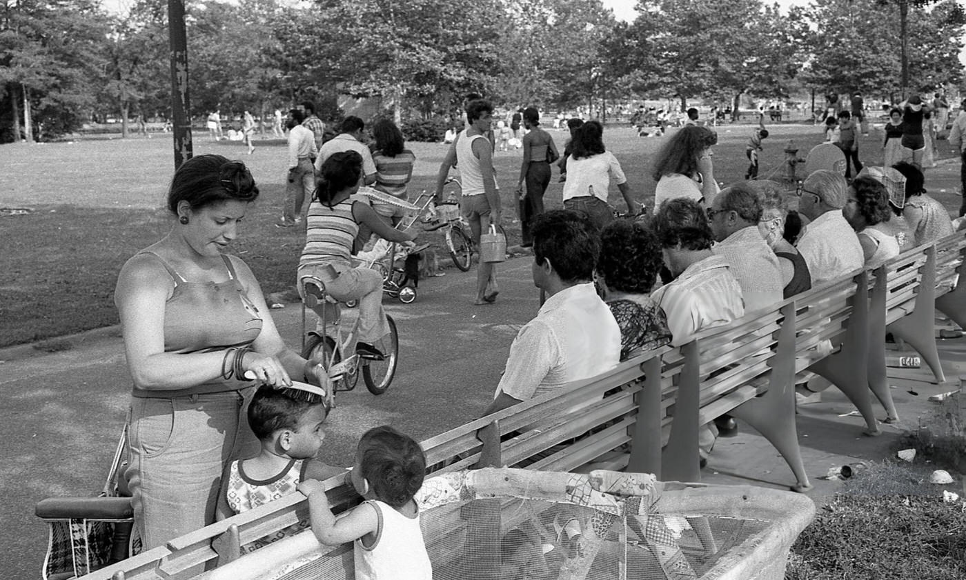 People Sit On A Park Bench As A Woman Combs A Child'S Hair In Flushing Meadows Park, Corona, Queens, 1980.