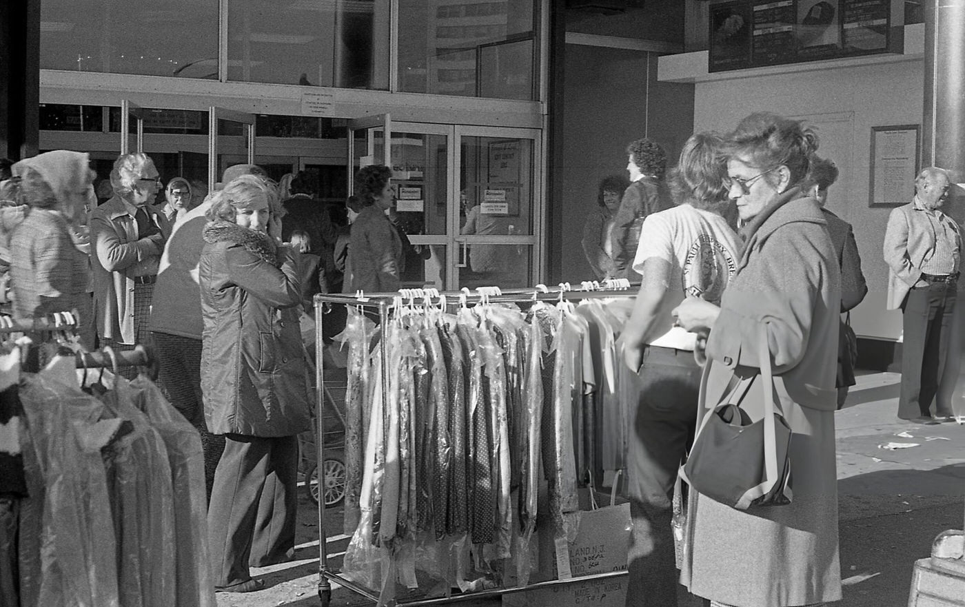 Pedestrians Look At Racks Of Clothing During A Sidewalk Sale On Queens Boulevard, 1980.