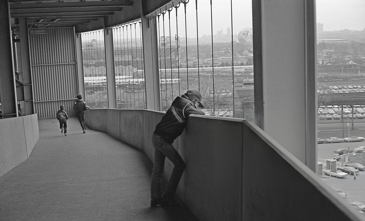 A Young Fan Looks Over The Edge Of An Elevated Pedestrian Walkway Over The Shea Stadium Parking Lot During A Baseball Game, Corona, Queens, 1982.