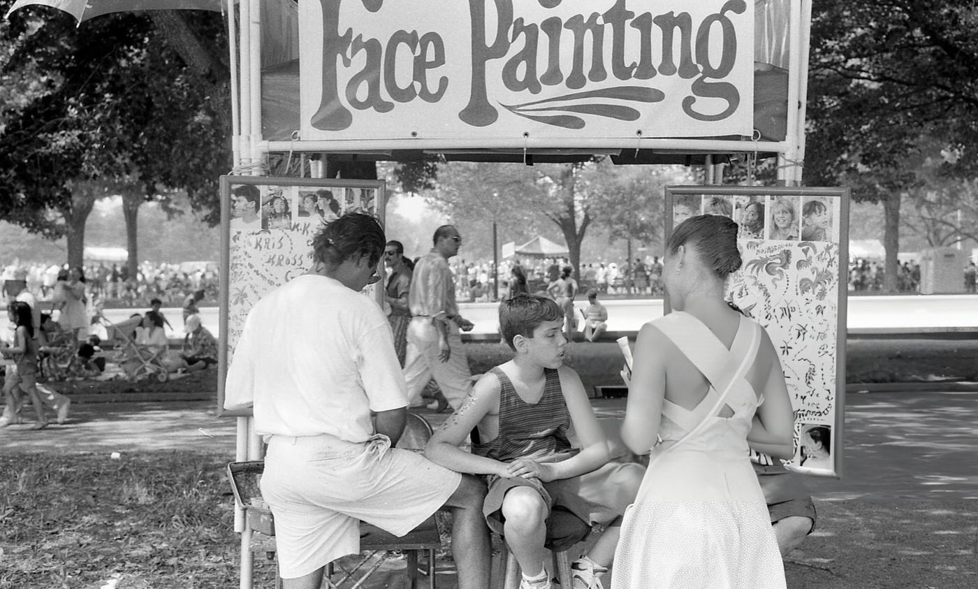 A Boy Sits Next To Two Make-Up Artists At A Face Painting Booth, Flushing Meadows Park, Queens, 1994.
