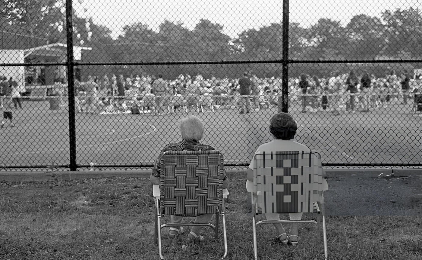 Two People Sitting Behind A Fence Watching A Free Concert In Juniper Valley Park In Queens' Middle Village Neighborhood, 1997.