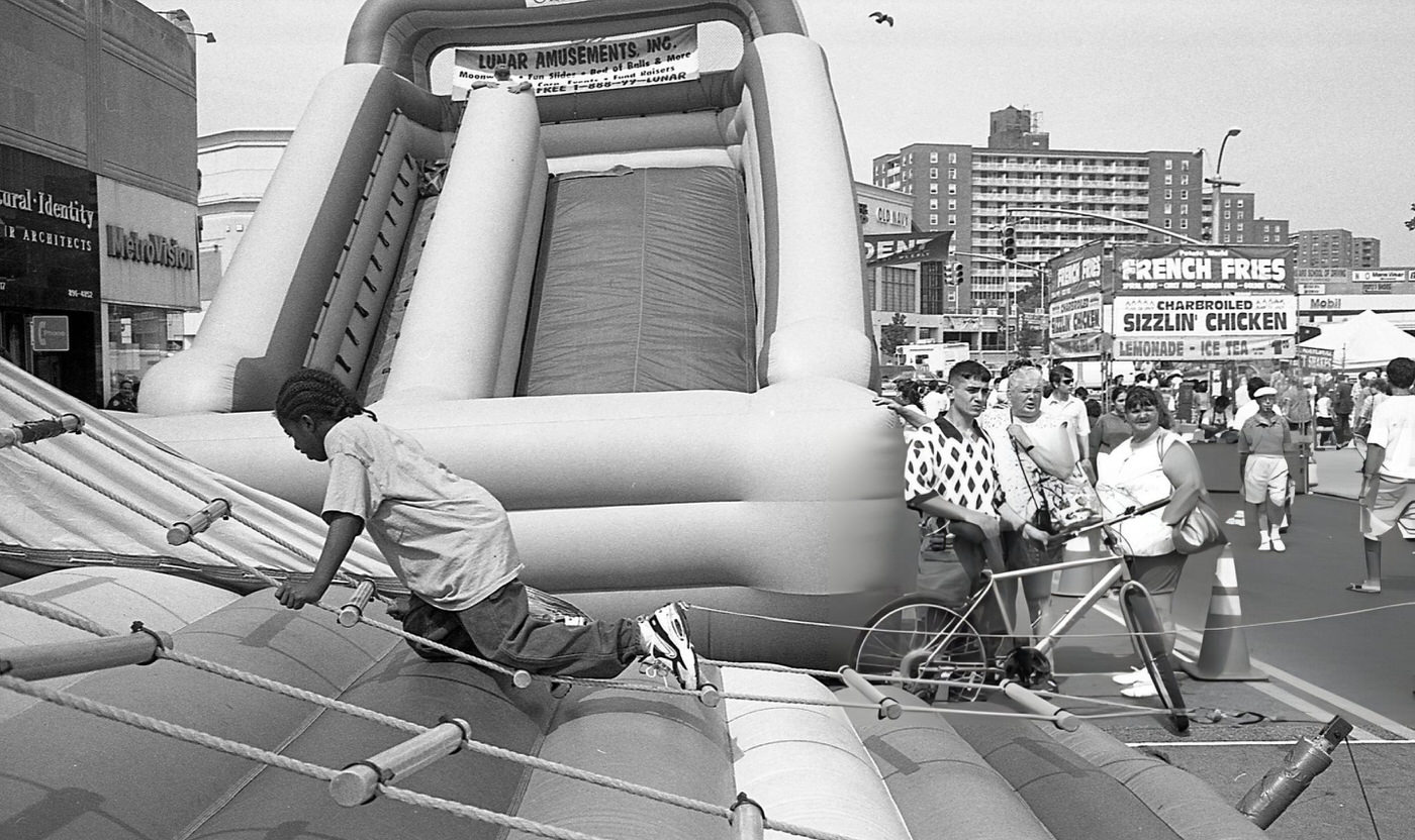 A Boy Climbs A Rope Ladder In Front Of An Inflatable Slide On 63Rd Drive During The 63Rd Drive Street Fair, Rego Park, Queens, 1997.