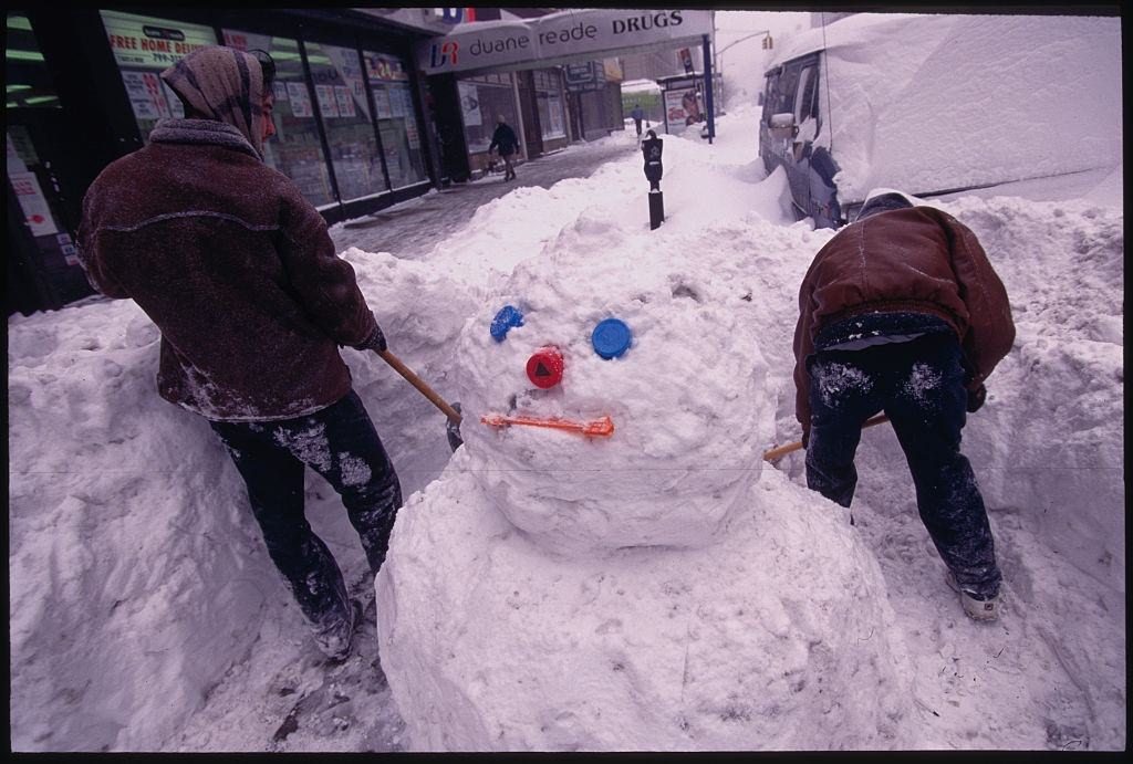 Two Men Shovel Snow Around A Snowman, 1996