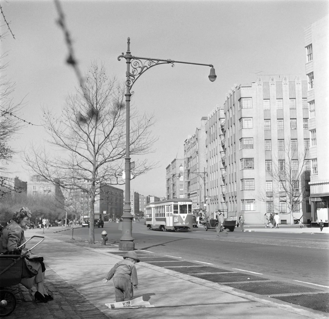 A Baby Plays On A Sidewalk As A Tramway Passes By, 1947.