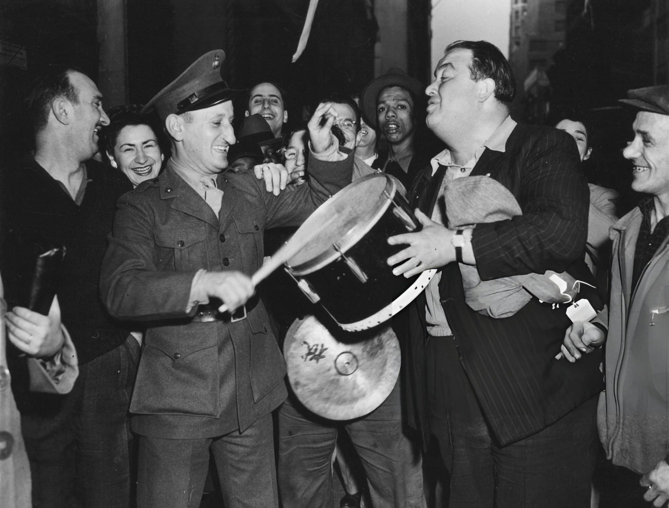 A Nighttime Portrait Of A Group Of People, Including A Man In Uniform Who Plays A Drum Held By A Second Man In A Pinstripe Jacket, Who Celebrate Ve Day, 1945.