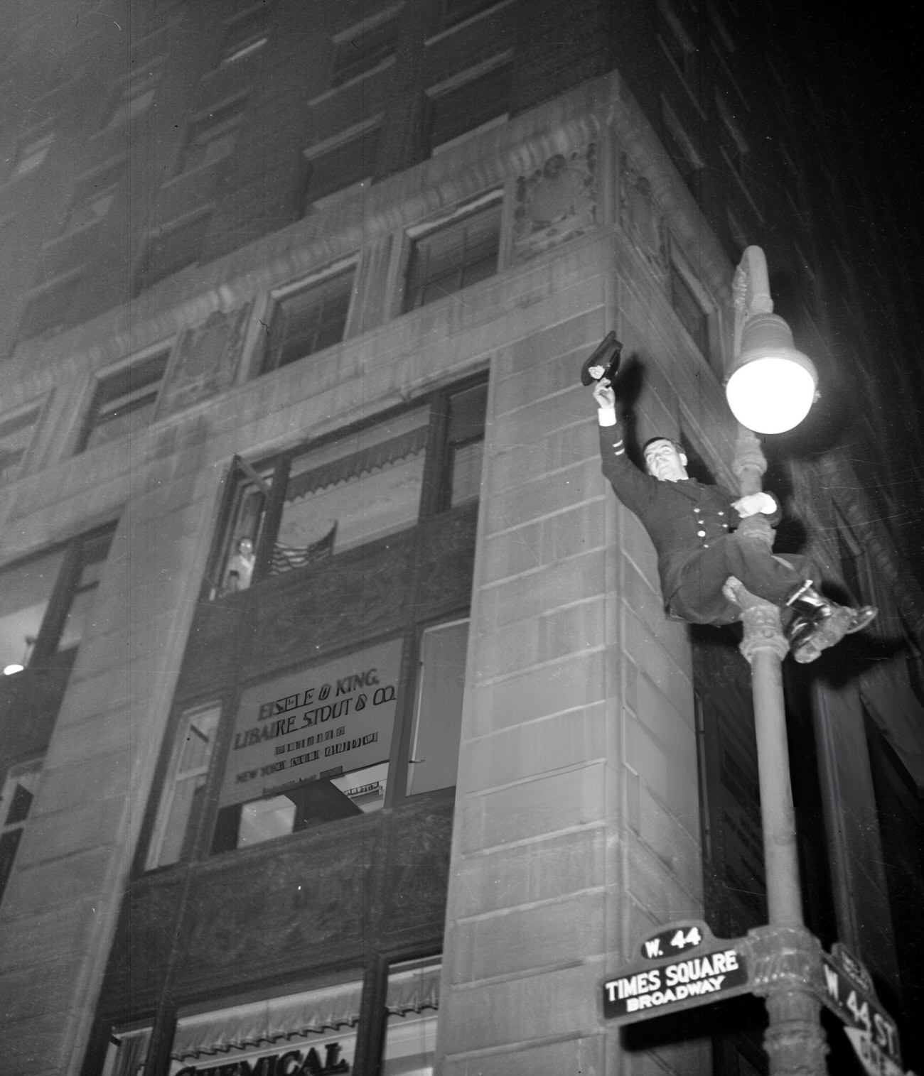 A Police Officer Waves His Cap From Atop A Street Lamp Pole At West 44Th Street And Broadway As He Celebrates V-E Day In New York, 1945.