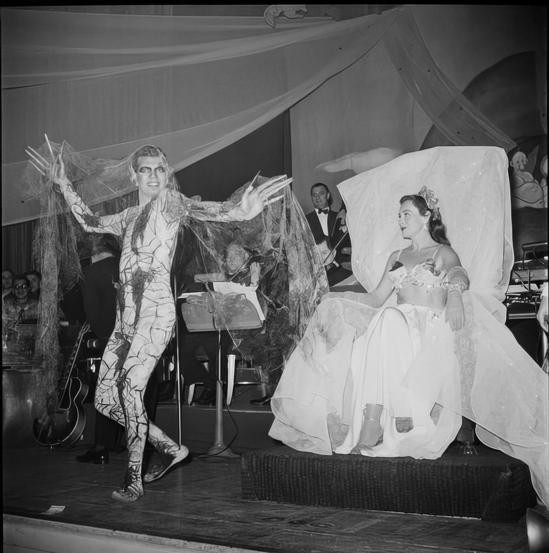 A man in an elaborate costume walking across the stage as a woman watches, 1951.