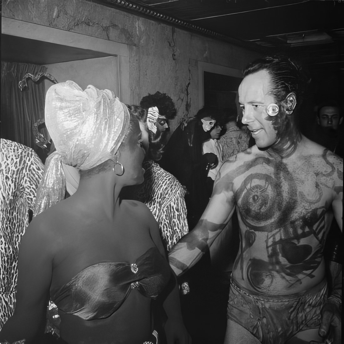 A man in body paint talking to a costumed woman, 1951.