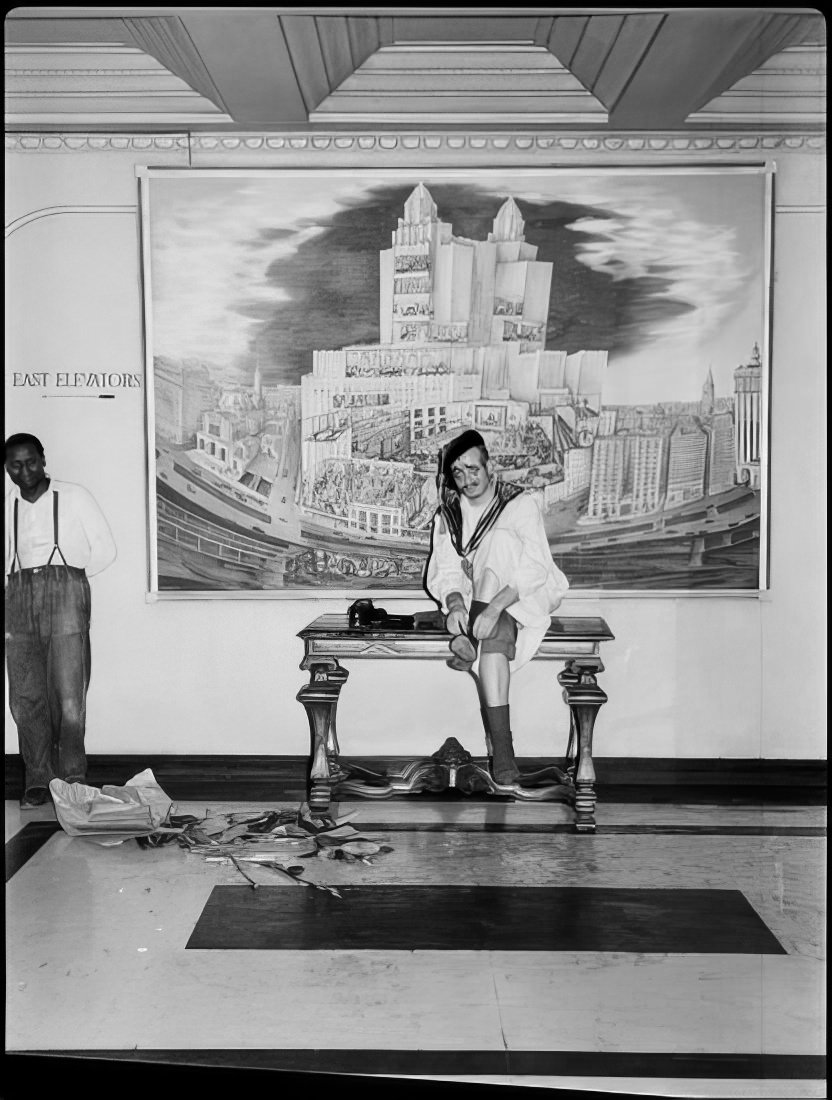 A man putting on shoes as he sits on a table in the hallway, 1951.