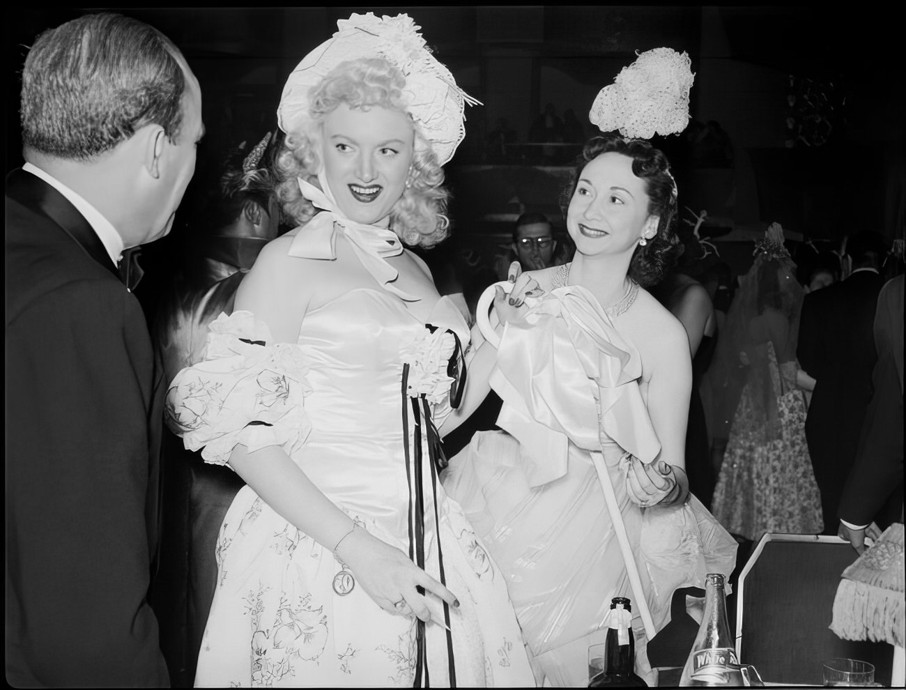 A man talking to two costumed women, 1951.