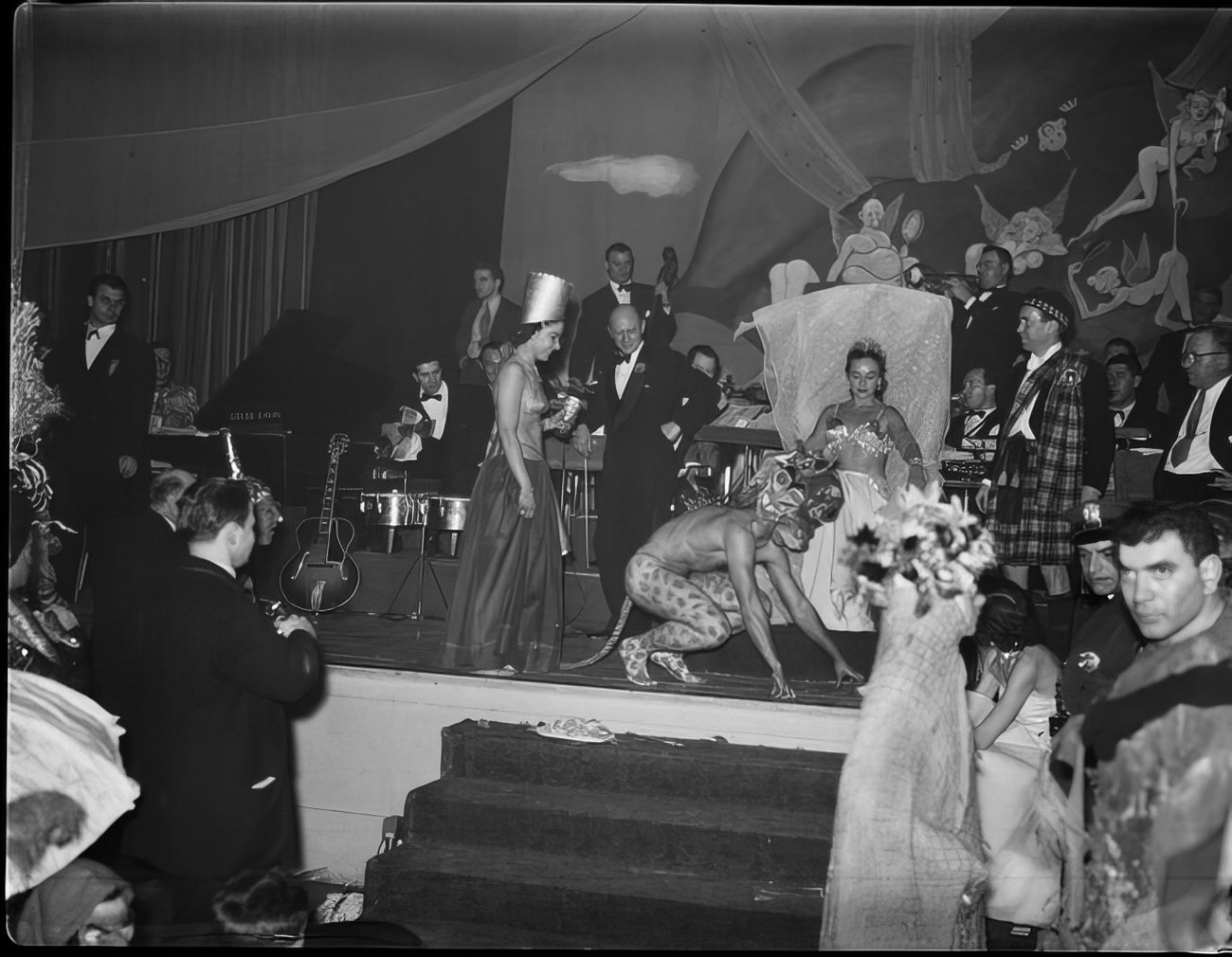 People in costume walking across the stage as a woman watches, 1951.