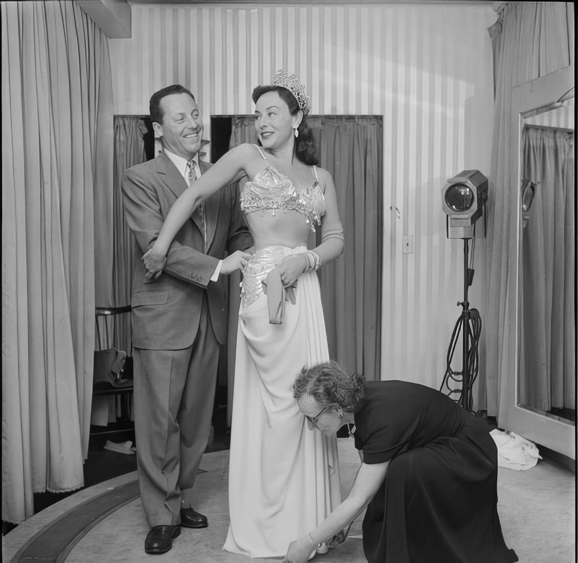 A woman getting her dress altered as a man helps and watches, 1951.