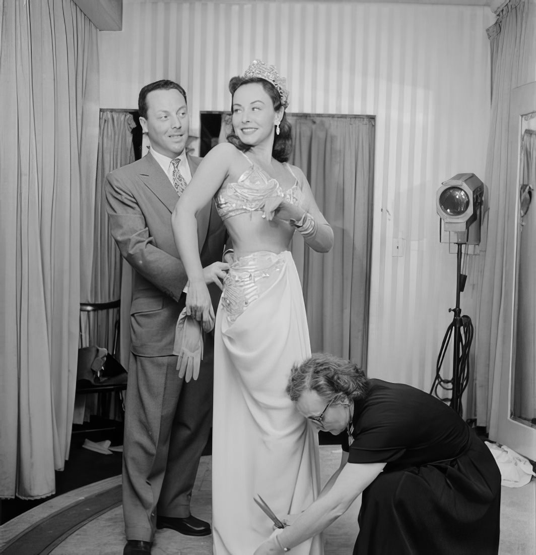 A woman getting her dress altered as a man helps and watches, 1951.